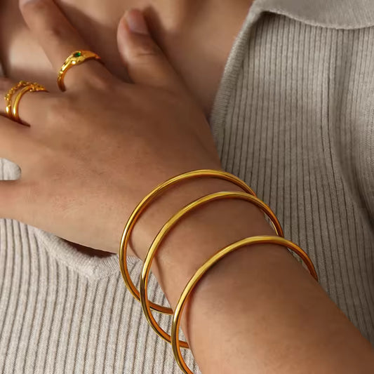 Close-up of a person's wrist wearing gold bracelets and rings on a neutral background